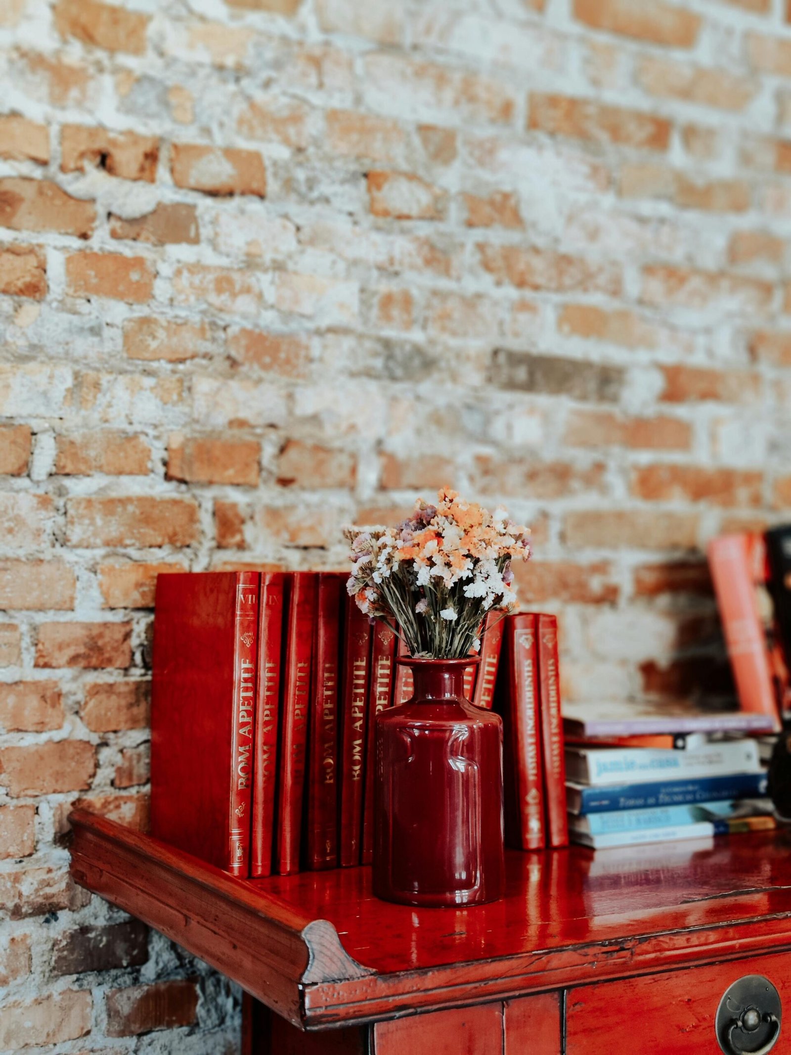 Small Flower Vase Set on Wooden Shelf in front of Books on Brick Wall